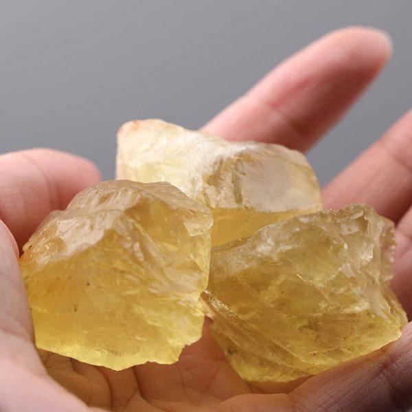 Genomskinlig gul resin-kristall, rå och naturlig, hålls mellan fingrarna. Perfekt för dekoration eller insamling av vetenskapliga objekt.