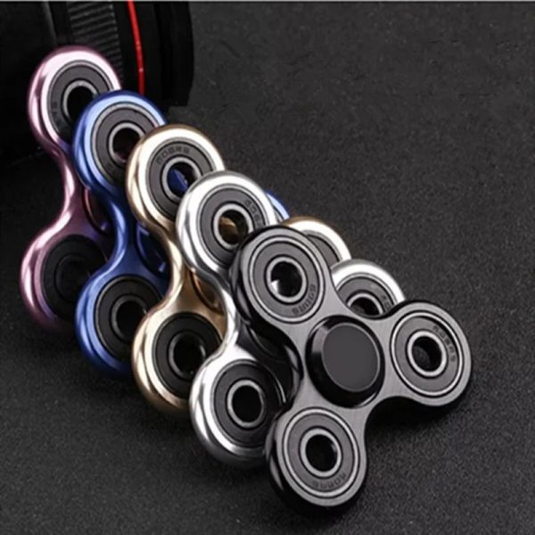 Handspinner i färgad metall med tre grenar, designad för avkoppling och underhållning, placerad på en mörk yta.