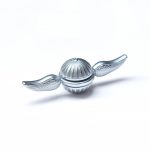 Liten silverfärgad metallkula med vingar, inspirerad av ett vetenskapligt eller dekorativt objekt, placerad på en vit bakgrund.