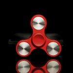Röd fidget spinner med tre grenar i glänsande metall, designad för avkoppling och underhållning, placerad på en svart bakgrund för att framhäva sina detaljer.