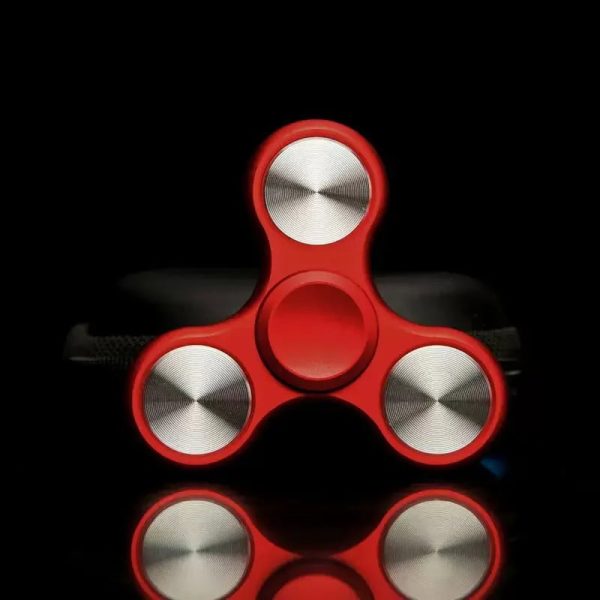 Röd fidget spinner med tre grenar i glänsande metall, designad för avkoppling och underhållning, placerad på en svart bakgrund för att framhäva sina detaljer.