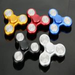 Antistressbalanser i anodiserad aluminium i olika färger (guld, röd, blå, svart, vit) på en glänsande svart bakgrund.