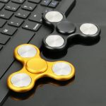 Fidget spinner i guld- och svart metall placerad på ett datorbord, som illustrerar ett modernt och trendigt vetenskapligt dekorationsobjekt.