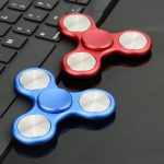 Två fidget spinners, en röd och en blå, placerade på ett datorbord, perfekta för avkoppling och koncentration.
