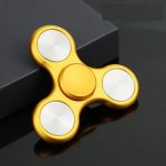 Snurrande fidget i guldmetall med tre grenar, designad för avkoppling och koncentration, placerad på en svart yta med en mörk bakgrund.
