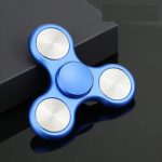 Blå fidget spinner med tre grenar och metalllager, placerad på en svart yta med mörk bakgrund.