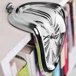 Deformerad väggklocka i glänsande metall med modern och konstnärlig design.