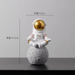 Dekorativ astronautfigur med gyllene hjälm, placerad på en stenmåne, idealisk för kontors- eller vetenskaplig inredning.