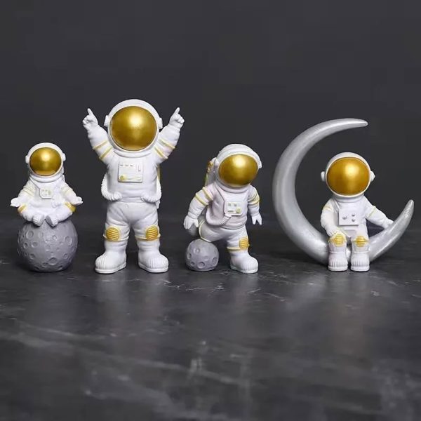 Fyra astronautfigurer i dekoration, med gyllene hjälmar och vita dräkter, tillsammans med en måne i dekoration, perfekta för ett rymd- eller vetenskapligt tema.