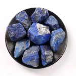 Rå lapis lazuli, naturliga blå stenar med vita och gyllene inklusioner, presenterad i en svart skål.