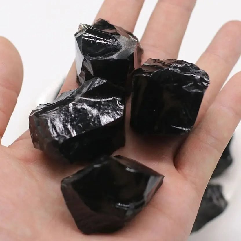 Rå svart obsidian, naturlig sten med skyddande och energigivande egenskaper, idealisk för dekoration eller litoterapi.