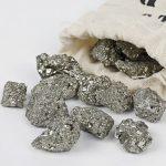 Glänsande och metallisk pyritnugget, från en vetenskaplig samling, placerad på en vit yta med en tygpåse i bakgrunden.