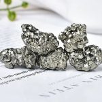 Grupp av naturliga pyritkristaller med glänsande metallisk yta, placerade på ett vitt papper, illustrerar mineralets skönhet och unika geologiska struktur.