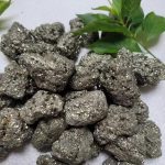 Grupp av pyritstenar med glänsande metalliska fläckar, tillsammans med gröna blad, på neutral bakgrund. Perfekt för vetenskaplig dekoration eller mineralinsamling.