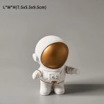 Liten vit astronautfigur i plysch med gyllene hjälm, idealisk för dekoration eller som vetenskaplig present till barn och rymdentusiaster.