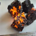 Fragment av meteorit med glänsande ytor och ljusa orange fläckar, som illustrerar den utomjordiska sammansättningen.