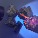 Meteorit under UV-ljus med orange och violett fluorescens.
