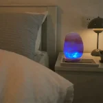 Naturlig stenlampa med blå LED-ljus, placerad på ett nattduksbord bredvid en säng, som skapar en modern och avslappnande atmosfär i sovrummet.