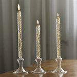 Tre transparenta glasljushållare med tända ljus, eleganta och moderna, placerade på ett träbord, som skapar en varm atmosfär.