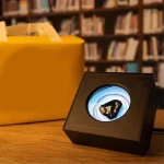 Liten låda med optiska illusioner med ett lysande cirkulärt mönster, placerad på ett träbord i ett bibliotek.