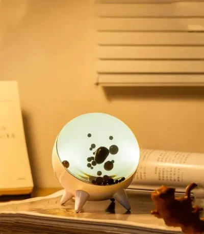 Skrivbordslampa i form av en planet med lysande yta och svarta detaljer, idealisk för vetenskaplig inredning eller en inspirerande arbetsyta.