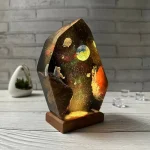 Resin-skulptur som föreställer ett rymdlandskap med planeter, astronauter och stjärnor, belyst för en galaktisk effekt.