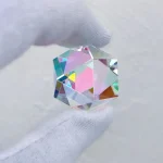Optisk glassten med färgade reflektioner, hålls varsamt mellan fingrarna.
