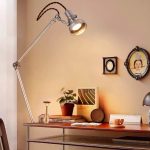 Vintage industriell skrivbordslampa med ledad arm i metall, belyser ett skrivbord med vetenskapliga och vintage-dekorationer.