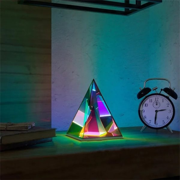 Vetenskaplig lampa i pyramidform med färgglad belysning, tillsammans med en vintage väckarklocka på ett träbord.