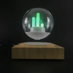 Dekorativ lampa i form av en kristallkula med grön ljusgrafik, placerad på en träbas, idealisk för vetenskaplig eller modern inredning.
