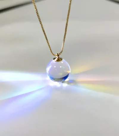 Halsband med transparent glasbollberlock, som fångar ljuset för att skapa en ljus och färgglad effekt. Perfekt för älskare av vetenskaplig dekoration och unika objekt.