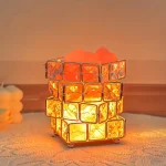 Bordslampa i orange glas i kubform som sprider ett varmt ljus.