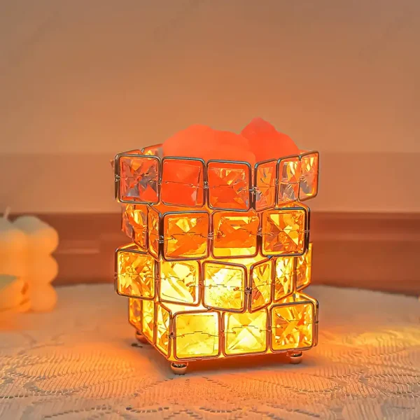 Bordslampa i orange glas i kubform som sprider ett varmt ljus.