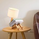 Bordslampa med staplade böcker som formar en mänsklig figur, placerad på ett träbord i en modern inredning.