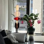 Blomvas med modern vetenskaplig dekoration, inklusive en blomsterarrangemang med gröna blad och rosa blommor, placerad nära ett fönster i en samtida inredning.