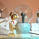 Dekorativ lampa i form av en planet med en astronautfigur, idealisk för vetenskaplig dekoration eller ett barnrum. Modern och lekfull design, perfekt för ett rymdtema.