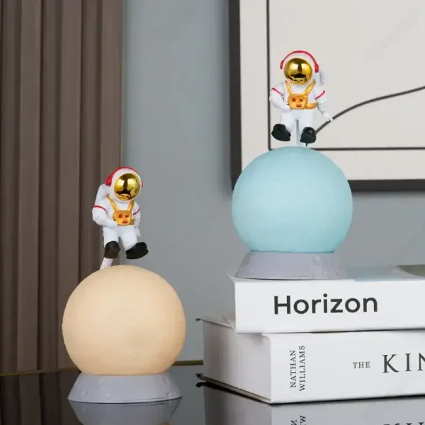 Två plastastronautfigurer med gyllene hjälmar, placerade på lysande sfärer, dekorerar en modern inredning med böcker i bakgrunden.