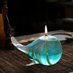 Glaskulptur som föreställer en val med ett tänd ljus inuti, placerad på en träyta.