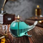 Dekorativ lampa i form av en narval i turkosa glas med tänd ljus, idealisk för vetenskaplig eller fantastisk dekoration.
