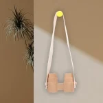 Hängande observationsglasögon i trä med vitt tygband, fäst vid väggen med en gul knapp, minimalistisk och naturlig dekoration.