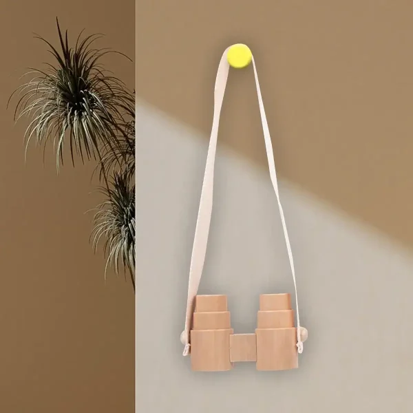 Hängande observationsglasögon i trä med vitt tygband, fäst vid väggen med en gul knapp, minimalistisk och naturlig dekoration.