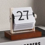Vintage klockkalender i trä och plast, visar datum 27, retrodesign för kontors- eller inredningsdekoration.