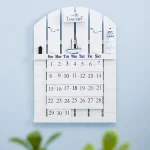 Vit trädkalender med marina inslag, inklusive en månadskalender, en båt, ett fyrtorn och fåglar, perfekt för en elegant inredning.
