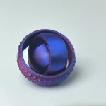 Tennisboll i målad metall i lila med texturerad yta, använd som dekorativt eller vetenskapligt objekt.