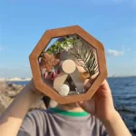 Hänge i trä med naturliga element, såsom blad och stenar, presenterat framför ett marint landskap. Perfekt för dekoration eller som en originalaccessoar inspirerad av vetenskap.