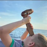 Barn som använder en vetenskaplig pult i trä med inbyggd förstoringsglas, vänd mot havet, för att utforska naturen och vetenskapen utomhus.