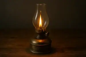 Gammaldags oljelampa i klart glas och metallbas, som mjukt lyser i mörkret.