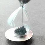 Sandklocka i glas med svart sand, symbol för tid och vetenskap, används som dekoration eller vetenskapligt objekt.