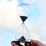 Vetenskaplig sandklocka i glas med svart sand, symbol för tid och precision, idealisk för kontors- eller vetenskapsinredning.