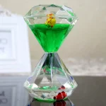 Transparent sandur hänge med grönt vätska, dekorerat med små färgglada figurer inuti, perfekt för dekoration eller som original nyckelring.